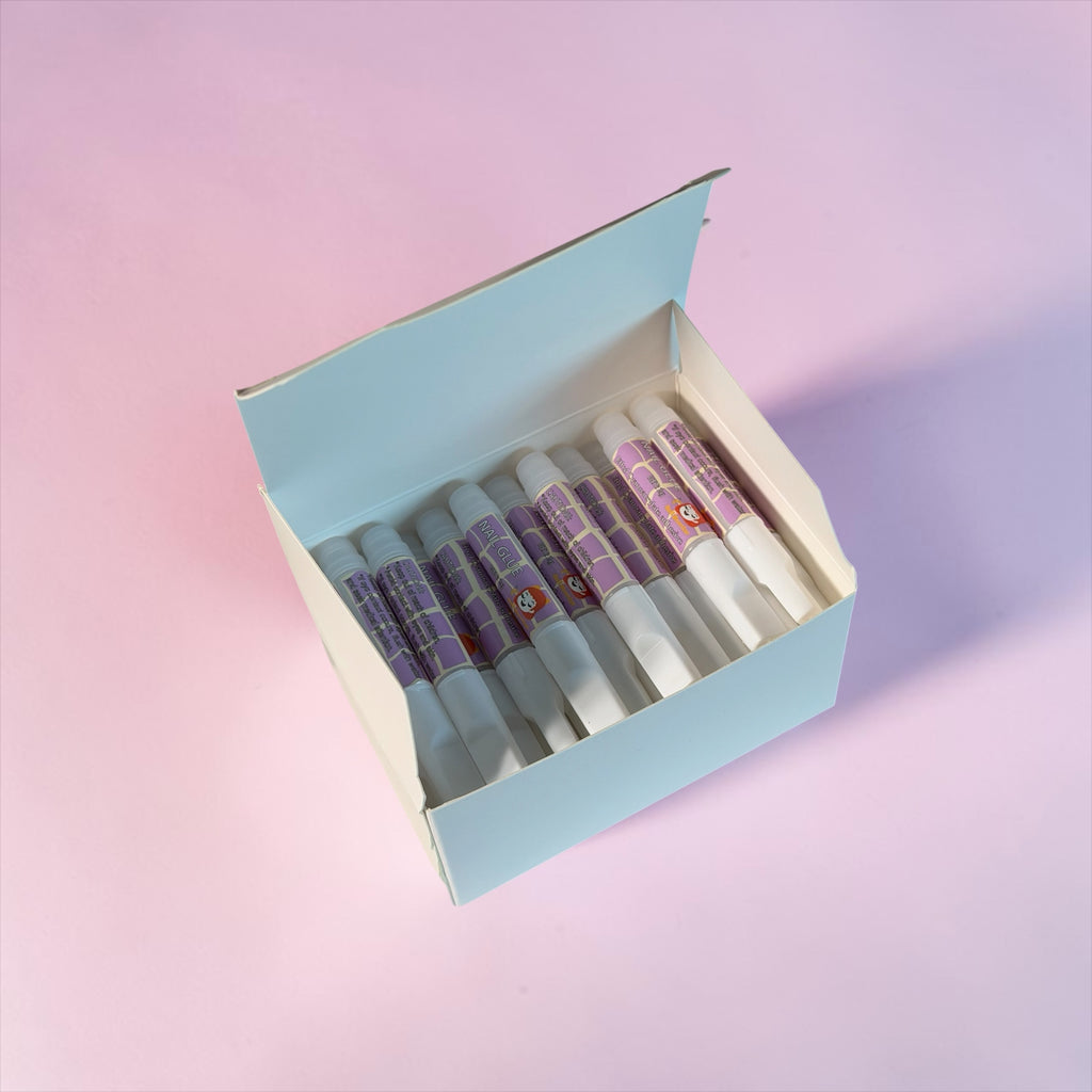 Nail Monsters professional adhesive nail glue pens in a light blue box on a pink background