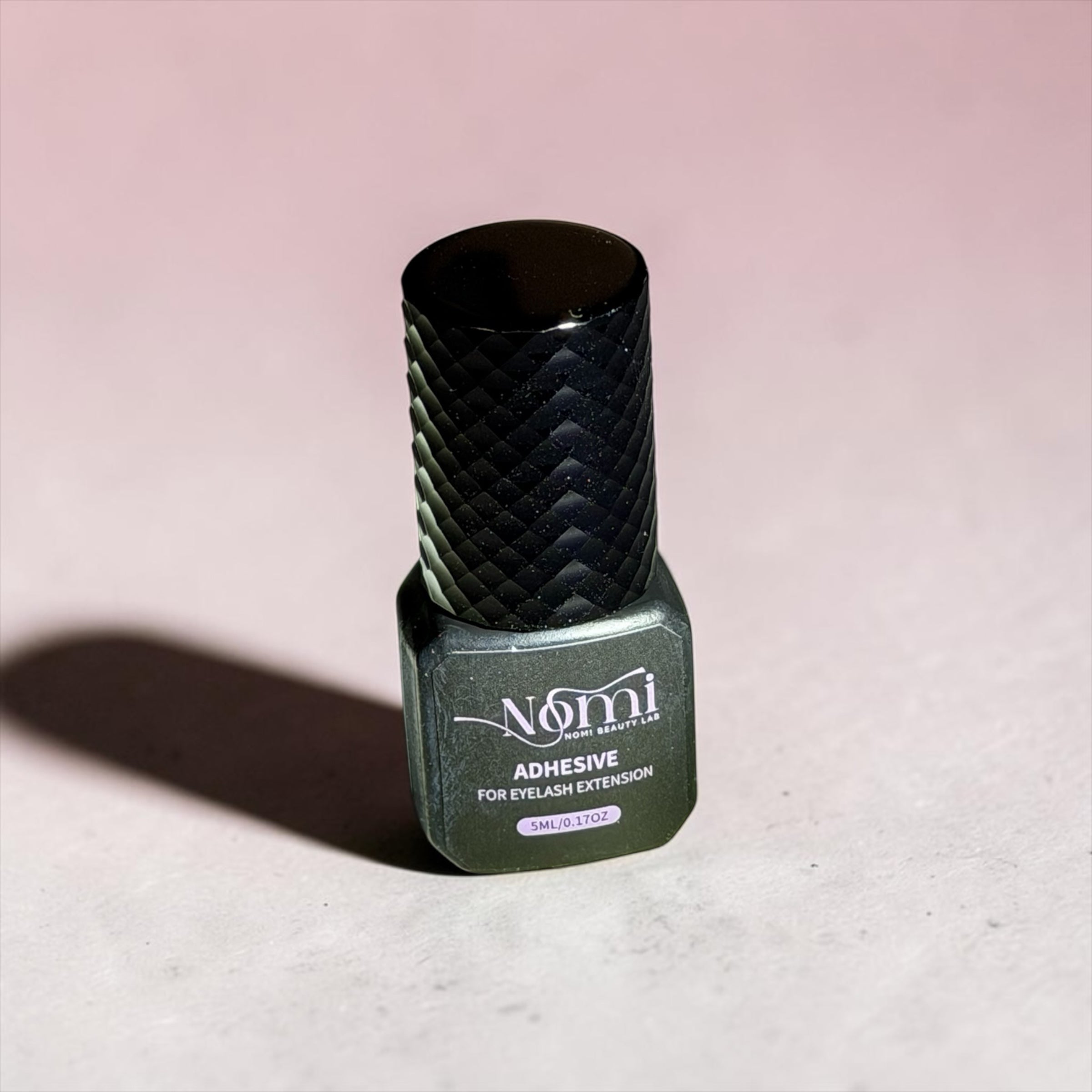 Nail Monsters Nomi Beauty Lab professional eyelash extension adhesive in a 5ml bottle with a textured black cap.