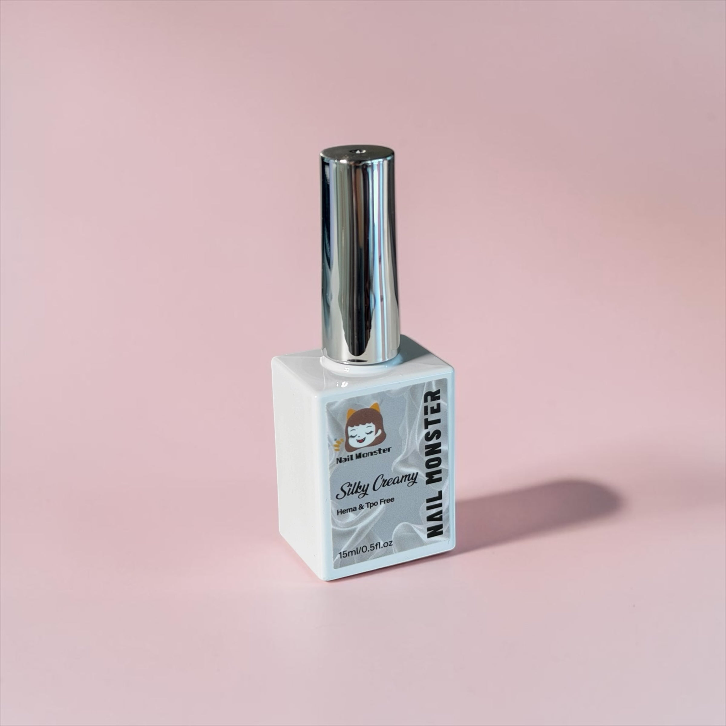 Nail Monsters Silky Creamy gel polish in a white 15ml bottle with a shiny silver cap on a soft pink background.