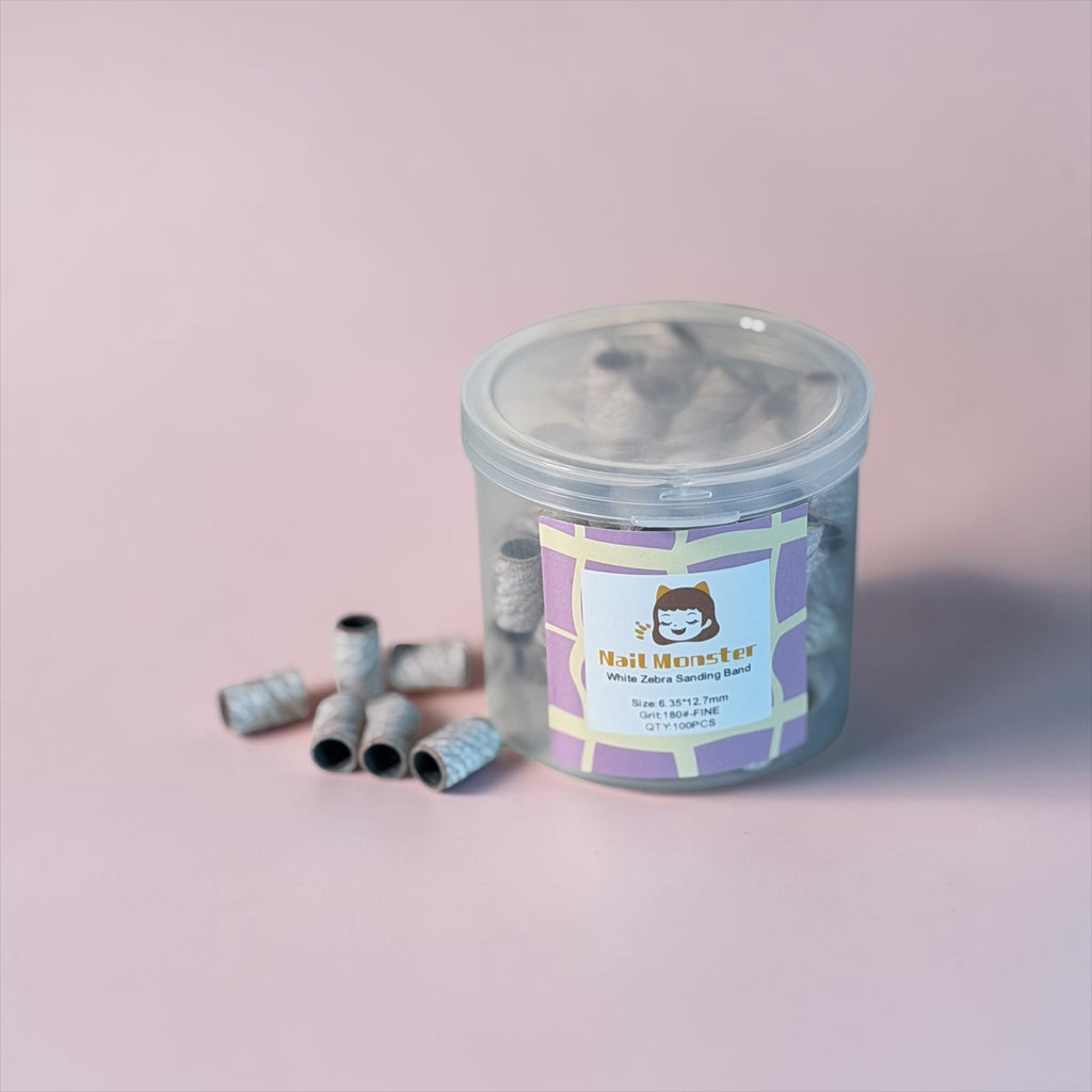 Nail Monsters 180-grit white zebra sanding bands in a clear storage jar for professional nail filing and buffing.